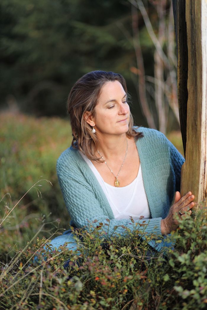 Anke Braun sitzt an einem Baum und schaut zur Seite