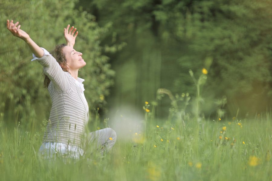 Barbara Wegener sitzt in einer Blumenwiese und streckt die Arme in den Himmel